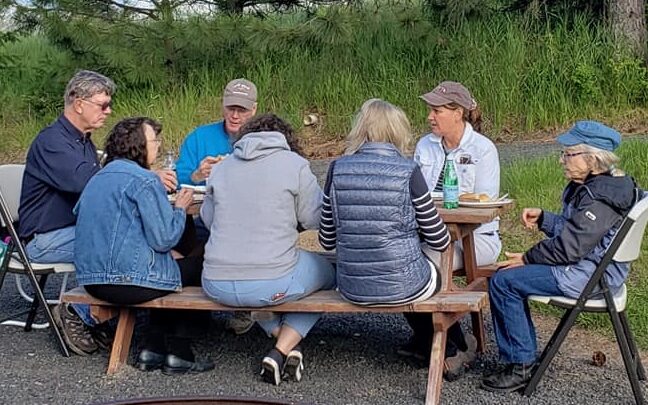 A small group shares a meal around a picnic table.